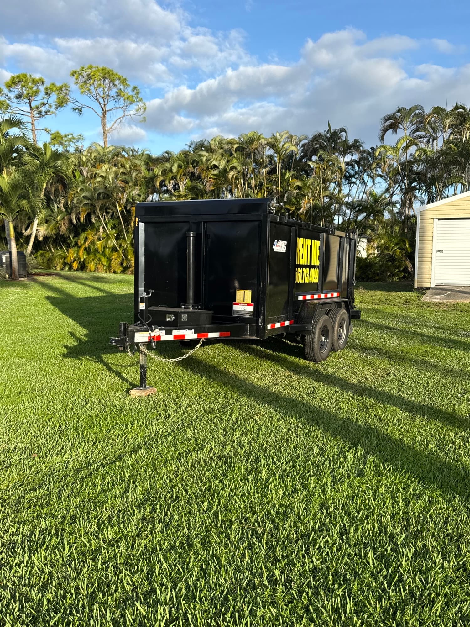 Dump trailer parked on a lawn lined with palm trees